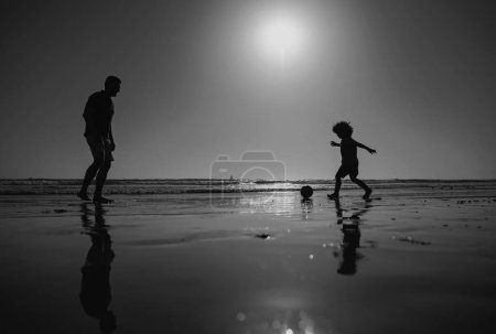 Photo for Father and son play soccer or football on the beach. Dad and child playing outdoor, silhouette on sunset. Active family concept - Royalty Free Image