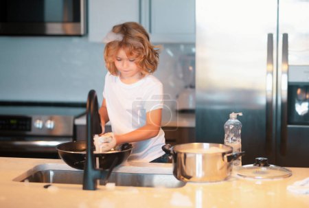 Photo for Child help in washing dishes at kitchen. Dishwashing liquid with a sponge on kitchen sink - Royalty Free Image