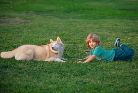 Foto de Niño niño juega con un perro en hierba al aire libre - Imagen libre de derechos