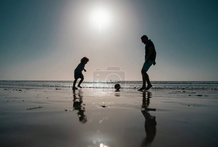 Foto de Padre e hijo juegan fútbol o fútbol en la playa en las vacaciones familiares de verano. Papi con niño jugando en un día de verano - Imagen libre de derechos