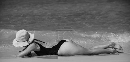 Photo for Summer vacation on sea. Girl sunbath near ocean. Woman in black swimwear lying on sand beach - Royalty Free Image