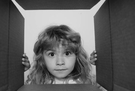 Téléchargez les photos : Joyeux petit garçon ouvre cadeau et regarder à l'intérieur de la boîte en carton. Parcelles et livraison - en image libre de droit