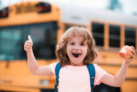 Téléchargez les photos : Un écolier excité dans le bus scolaire. Enfant avec un geste positif avec la main, les pouces levés souriant et heureux - en image libre de droit