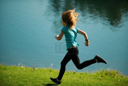 Téléchargez les photos : Enfant garçon jogging dans le parc en plein air. Sport pour enfants, joyeux jogging pour enfants actifs à l'extérieur, course au parc printanier. Jogging matinal - en image libre de droit