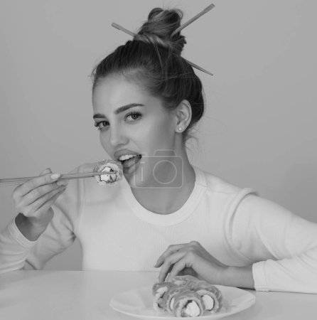 Foto de Japanese sushi style. Sexy woman eat japanese traditional food sushi rolls. Girl is holding japanese sushi piece of roll philadelphia by chopsticks - Imagen libre de derechos
