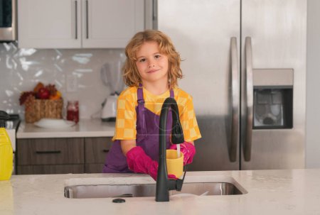Foto de Limpie los platos lavados, lavavajillas líquido con espuma. Servicio de limpieza de ayuda infantil. Niño barrer y limpiar platos en la cocina - Imagen libre de derechos