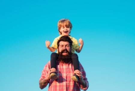 Photo for Portrait of happy father giving son piggyback ride on his shoulders. Cute boy with dad playing outdoor. Kid son hugging father against sky. Generations family - Royalty Free Image