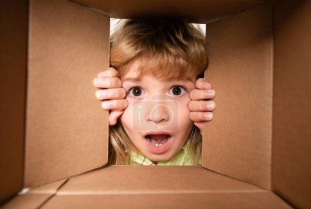 Foto de Desempacar la caja de cartón para niños. Alegre niño lindo abriendo un regalo. Vista desde dentro de la caja. Primer plano niños cara - Imagen libre de derechos