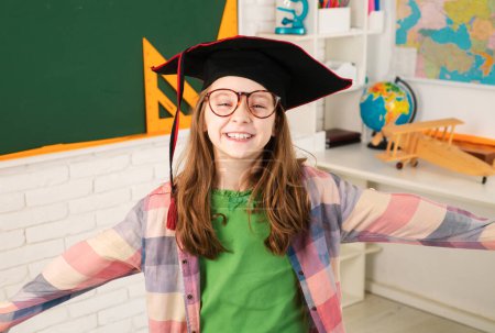 Téléchargez les photos : Portrait d'écolière heureuse avec chapeau de fin d'études en classe - en image libre de droit