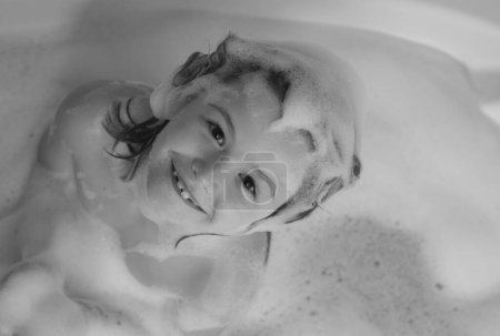 Photo for Kids shampoo. Foam on child head. Kid having fun in the bath with bubbles. Happy child enjoying bath time. Little boy smiling in the bath with soap foam. Child bathes in a bath with foam - Royalty Free Image
