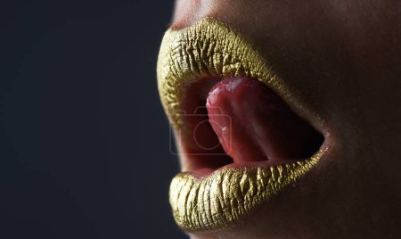 Téléchargez les photos : La langue sexy lèche les lèvres. Style brillant pour lèvres sexy. Des lèvres de femme sensuelle. Bouche dorée de luxe. Des lèvres d'or glamour. Lèvres dorées avec peinture dorée ou rouge à lèvres métallique - en image libre de droit