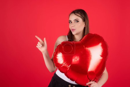 Photo for Beautiful young woman with heart shape air balloon on studio isolated background. Woman on Valentines Day. Heart of love. Girl hold red balloons heart. Holiday party, birthday. Heart love concept - Royalty Free Image