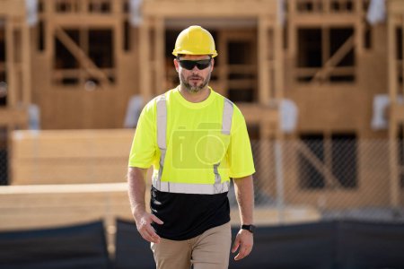 Photo for Construction site worker in helmet working outdoor. A builder in a safety hard hat at constructing buildings. American wooden house in beams, wood frame structure, framing construction - Royalty Free Image