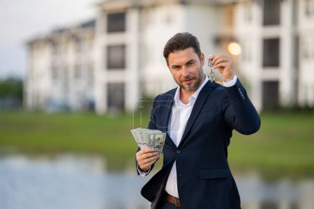 Photo for Realtor with money dollars and house keys against the background on new apartment home. Realtor in suit demonstrating keys and cash, outdoor portrait. Realtor offering new home. Property concept - Royalty Free Image
