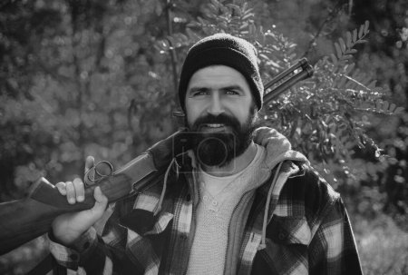 Téléchargez les photos : Un chasseur barbu tenant une arme et marchant dans la forêt. Chasseur avec fusil de chasse en chasse. Automne saison de chasse - en image libre de droit