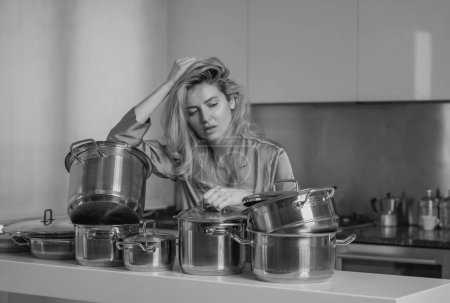Foto de Mujer aburrida con muchas ollas de cocina en la cocina por la mañana. Mañana de mujer ama de casa - Imagen libre de derechos