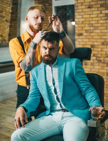 Téléchargez les photos : Homme en visite chez le coiffeur chez le coiffeur. Coiffeur professionnel à l'intérieur du salon de coiffure. Barbier - Rasages et garnitures. Coiffure et coiffeur - en image libre de droit