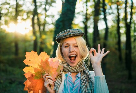 Foto de Feliz niña de otoño guiñando el ojo. Chica de otoño usando en ropa de otoño y se ve muy sensualmente. Chica jugando con hojas en otoño hojas de fondo - Imagen libre de derechos