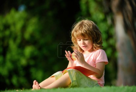 Photo for Distance children education. Cute little boy studying and eating apple outside in park - Royalty Free Image