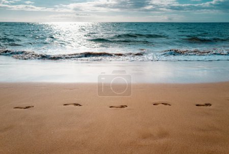 Fußabdrücke im Sand bei Sonnenuntergang. Tropischer Sandstrand mit Meereswellen. Schritte am Ufer