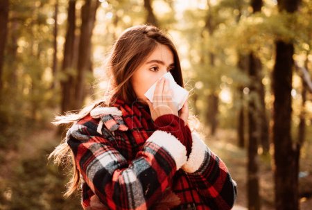 Photo for Young woman with nose wiper near autumn tree. Sick girl with runny nose and fever. Showing sick woman sneezing at autumn park. Young woman having flu and blowing her nose - Royalty Free Image