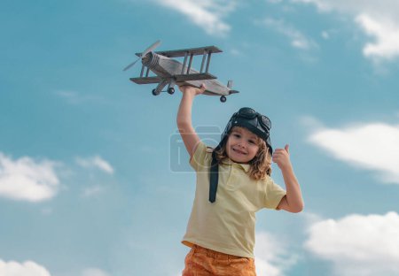 Téléchargez les photos : Enfant garçon avec lunettes de pilote et casque jouant avec un avion jouet en bois. Des rêves d'avenir. Pilote rêvant. Concept de rêve d'enfance. Blonde enfant rêveur mignon rêve à la volée - en image libre de droit