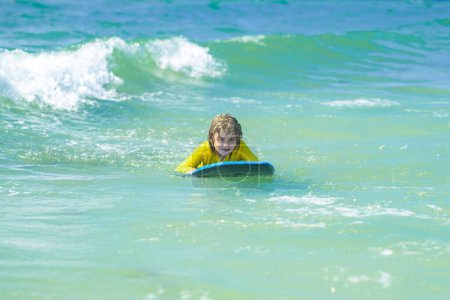 Foto de Los pequeños surfistas aprenden a montar en la tabla de surf en las olas del mar. Vacaciones infantiles de verano en sat. Vacaciones de verano con niños. Surfista niño está montando una ola. Niño aprendiendo a surfear en el mar o en el océano - Imagen libre de derechos