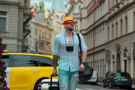 Foto de Turista caminando por la calle de la ciudad. Retrato del hombre de la moda con equipaje, maletas de vacaciones. Estilo de vida. Hombre con bolsa de viaje listo para viajar en sus vacaciones - Imagen libre de derechos
