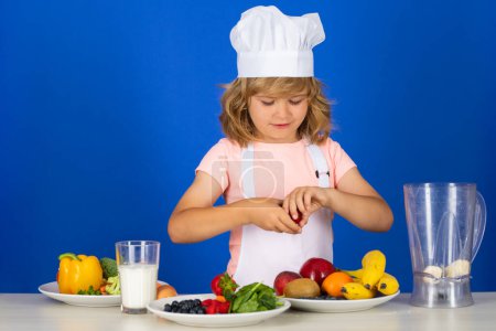 Téléchargez les photos : Enfant chef habillé tablier de boulanger et chapeau de chef isolé sur fond de studio. Alimentation saine pour enfants - en image libre de droit