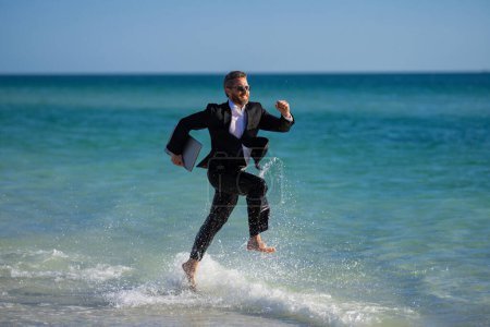Photo for Summer business. Freelancer on summer sea beach. Business man in wet suit in sea water. Crazy business vacation. Funny businessman with laptop in formal wear near tropical beach. Hot business summer - Royalty Free Image