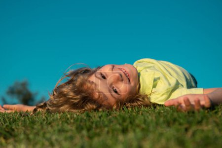 Téléchargez les photos : Garçon joyeux allongé sur l'herbe verte. Concept de liberté et d'imagination. Un rêve d'été. Des rêves d'enfant sur l'herbe. Rêve d'enfance. Enfant rêveur. Rêves et imagination. Visage d'enfant rêveur - en image libre de droit