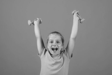 Photo for Child girl is doing exercises with dumbbells on yellow studio background. Sport portrait kids - Royalty Free Image