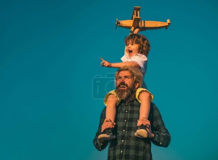 Téléchargez les photos : Garçon avec un avion jouet assis sur les épaules des pères. Enfant et papa jouent. Enfant pilote aviateur et papa rêve de voyager - en image libre de droit