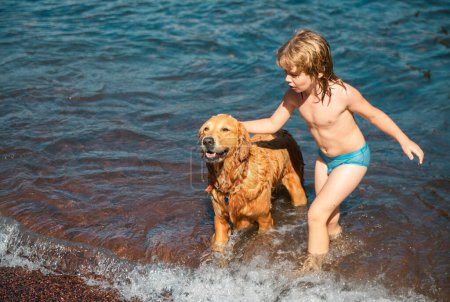 Foto de Niño feliz jugando con el perro en la playa. Niño jugando con el perro en el agua - Imagen libre de derechos