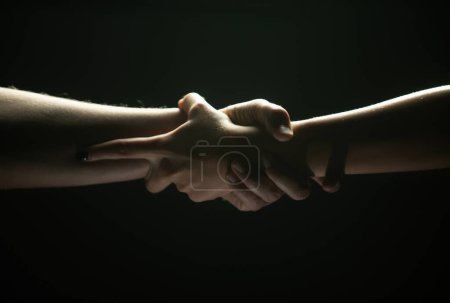 Mains geste sur fond noir. Un coup de main. Soutien et aide, salut. Force des mains fortes de deux personnes au moment du sauvetage. Aider la main tendue pour le salut. Forte emprise