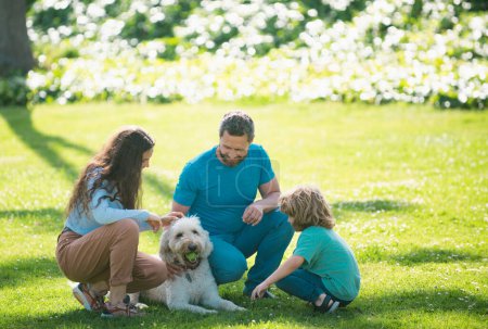 Foto de Familia relajante en el jardín con perro mascota. El concepto de una familia feliz. Padres e hijos de vacaciones jugando juntos al aire libre - Imagen libre de derechos