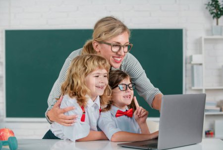 Photo for First day at school. Cute little boy from elementary school and tutor teacher studying lesson on laptop in class. Teacher and little students portrait, teachers day - Royalty Free Image