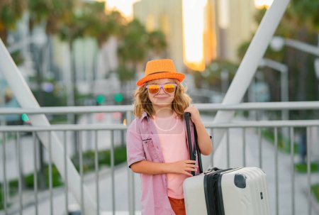 Foto de Concepto de viaje. Niño feliz turista con viaje bolsa de viaje. Niño con maleta viajando en la calle de la ciudad al aire libre - Imagen libre de derechos