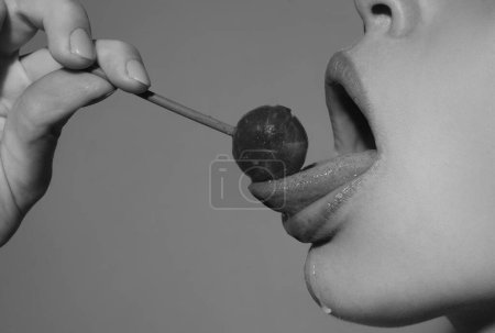Photo for Licking tongue lips. Girl with sexy mouth eating chupa chups close up. Woman lips sucking lollypop. Woman holding lollipop in mouth, close up. Red lips, sensual and sex shop concept - Royalty Free Image