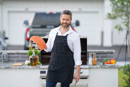 Photo for Chef in cook apron preparing salmon fish on barbecue grill outdoor. Man cooking tasty food on barbecue grill at backyard. Chef preparing seafood on barbecue. Bbq party. Fish grilling - Royalty Free Image