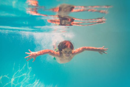 Téléchargez les photos : Le gamin nage sous l'eau dans la piscine d'été. Concept vacances d'été pour enfants. Les enfants drôles font face sous l'eau. Des éclaboussures d'enfants dans la piscine. Sports nautiques d'été. Vacances d'été avec enfant - en image libre de droit