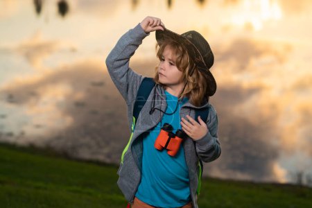 Téléchargez les photos : Scout boy portant un chapeau explorateur et un sac à dos en plein air. Explorer et aventure avec binoculaire - en image libre de droit