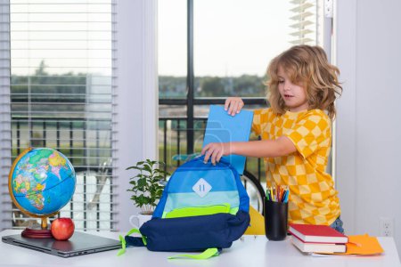 Photo for School kid student puts school supplies in a backpack. Preparation for school. Elementary school child doing homework in room. Nerd pupil studying at home - Royalty Free Image