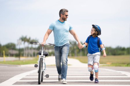 Foto de Seguridad en carretera. Cruce peatonal para ciclistas. Día de los Padres. Padre enseñando a su hijo a montar en bicicleta. Padre e hijo en bicicleta en el día de verano. Padre sostenga al niño. Padres amor - Imagen libre de derechos
