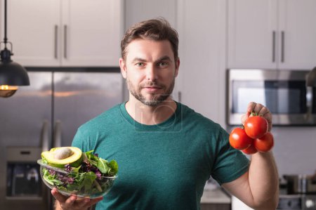 Photo for Man in modern kitchen, preparing healthy food alone, cooking salad. Handsome man is preparing fresh vegan salad in the kitchen at home. Healthy food is healthy life - Royalty Free Image