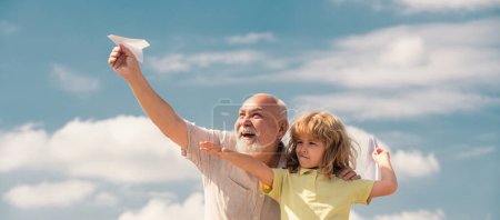 Téléchargez les photos : Petit-fils enfant et grand-père jouant avec avion en papier sur fond de ciel d'été. Enfant garçon avec des rêves de voler ou de voyager - en image libre de droit