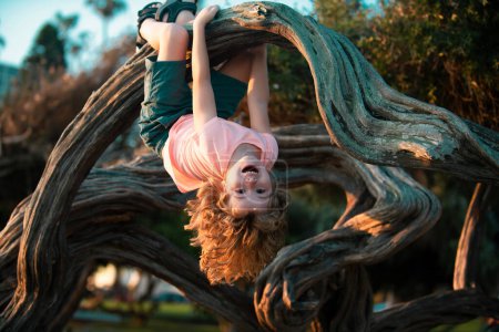 Téléchargez les photos : Enfant grimpant à l'arbre. Sourire drôle enfant clim arbre dans le jardin - en image libre de droit