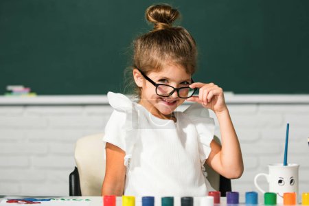 Foto de Linda cara de chica de la escuela con gafas. Niñas haciendo dibujos coloridos con lápices de colores en el aula de la escuela. Pintando niños - Imagen libre de derechos