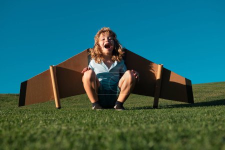 Photo for Child flying in plane made craft of cardboard wings. Dream, imagination, childhood. Travel and summer vacation concept. Smiling kid dreaming about summer vacation and travel - Royalty Free Image