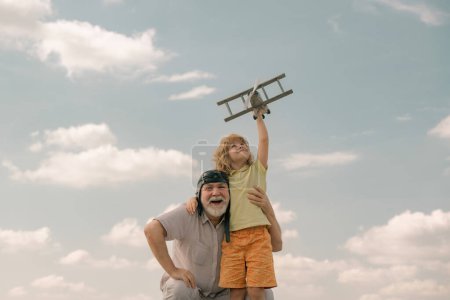 Téléchargez les photos : Enfant garçon et grand-père avec avion jouet sur fond bleu ciel et nuages. Hommes génération grand-père et petit-fils jouer à l'extérieur - en image libre de droit